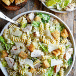 Chicken Caesar Pasta Salad with rotini, lettuce, chicken, croutons, and parmesan in a white bowl on a rustic wood table.