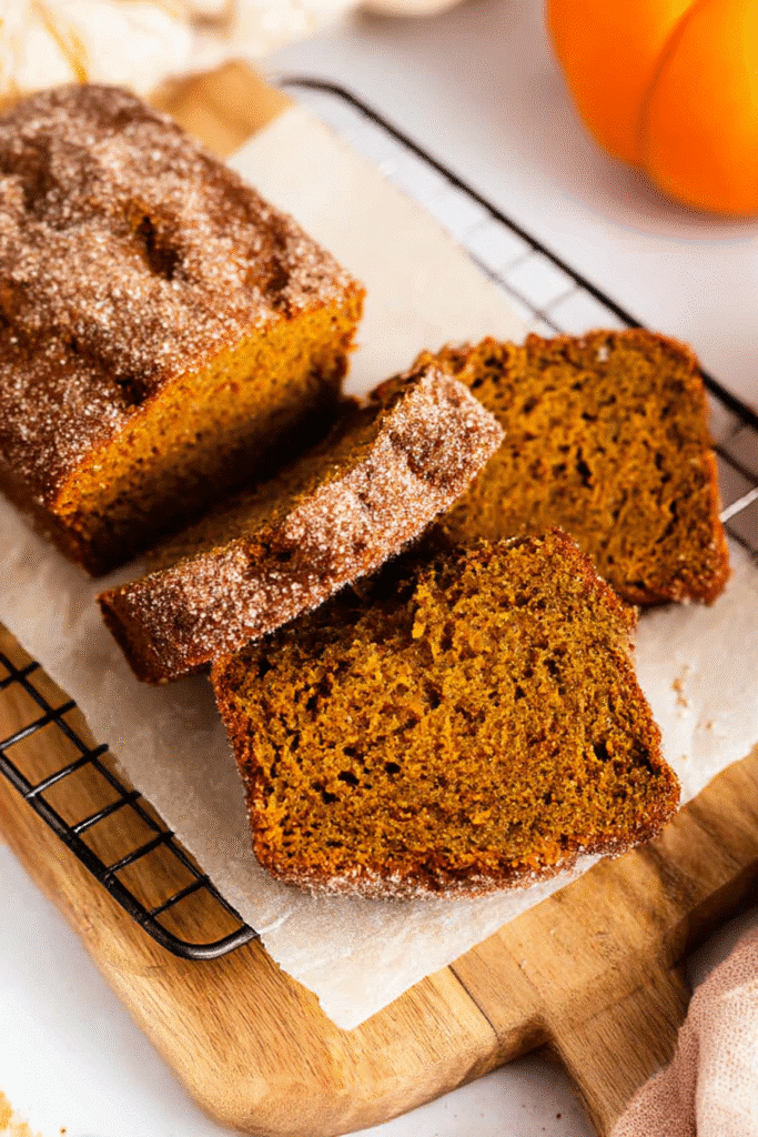 Sliced cinnamon swirl pumpkin bread loaf on a wooden board. Homemade dessert with cinnamon sugar crust.