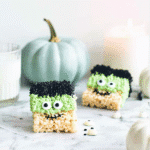 Frankenstein-themed halloween rice krispie treats with green frosting and candy eyes on a white background.