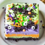 Top-down view of a Halloween lush dessert with candy eyeballs, colorful sprinkles, and green whipped topping over purple and orange mousse layers.