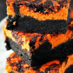Stack of Halloween swirl cream cheese brownies with vivid orange filling and black marbled brownie layers.