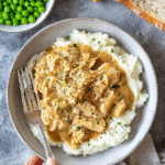 Homestyle chicken and gravy served over creamy mashed potatoes with bread and peas.