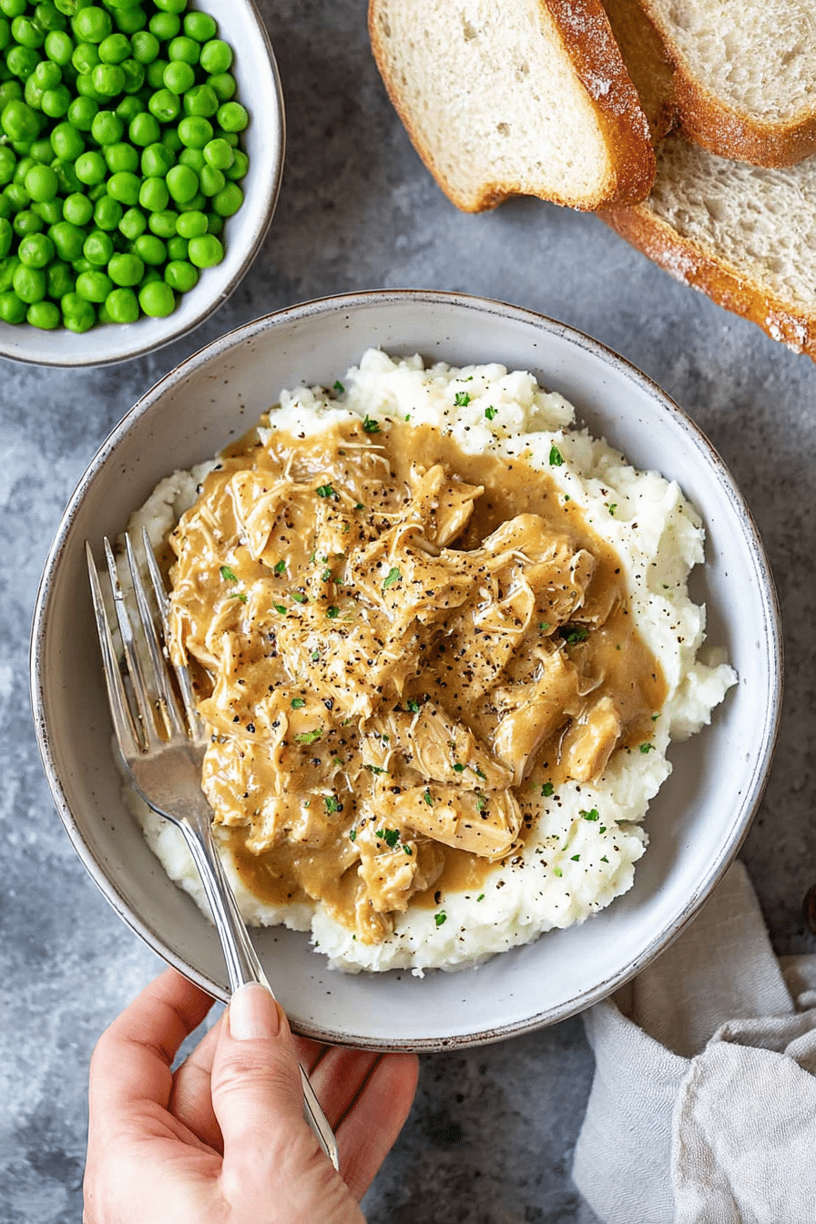 Homestyle chicken and gravy served over creamy mashed potatoes with bread and peas.