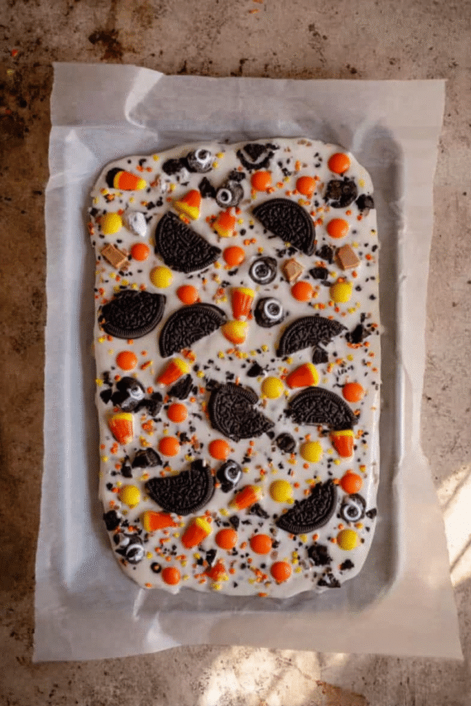 White Chocolate Halloween Oreo Bark topped with Oreos, Reese’s Pieces, candy eyes, and sprinkles before chilling