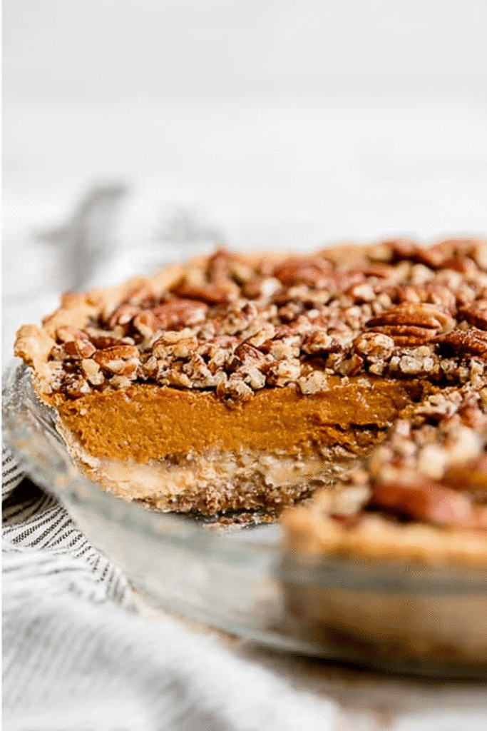 Sliced praline pumpkin pie in a glass dish showing layers of pumpkin custard and pecan topping.