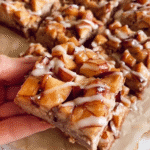 Gooey brown butter apple bars topped with cinnamon glaze, set on parchment over a marble surface.