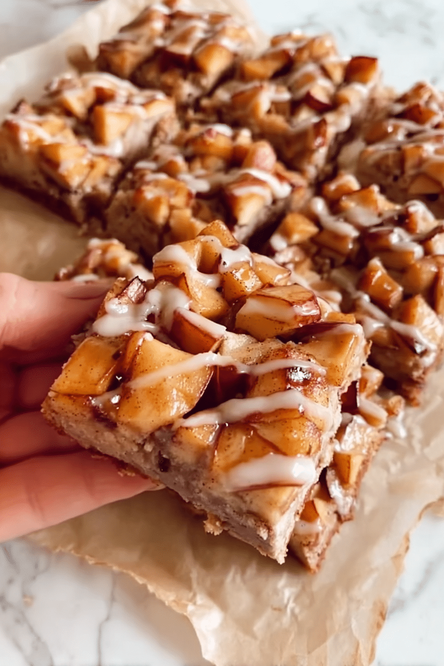 Gooey brown butter apple bars topped with cinnamon glaze, set on parchment over a marble surface.