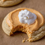 Close-up of a Crumbl Pumpkin Pie Cookie with creamy pumpkin frosting and whipped cream on parchment paper.