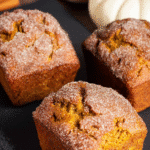 Sliced cinnamon swirl pumpkin bread loaf on a wooden cutting board. Homemade mini loaves with a sugar crust.