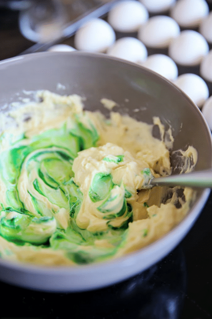 Mixing deviled egg filling with bright green food coloring for Halloween deviled eggs, with marble-veined egg whites in the background.