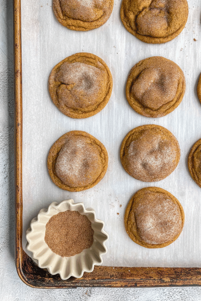 Overhead view of pumpkin cheesecake snickerdoodles on a white tray with a bowl of cinnamon sugar, showcasing their golden-brown texture and fall dessert charm.