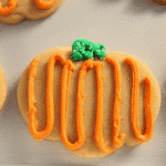 Pumpkin-shaped sugar cookie with orange frosting and green stem, perfect for pumpkin spice sugar cookies.