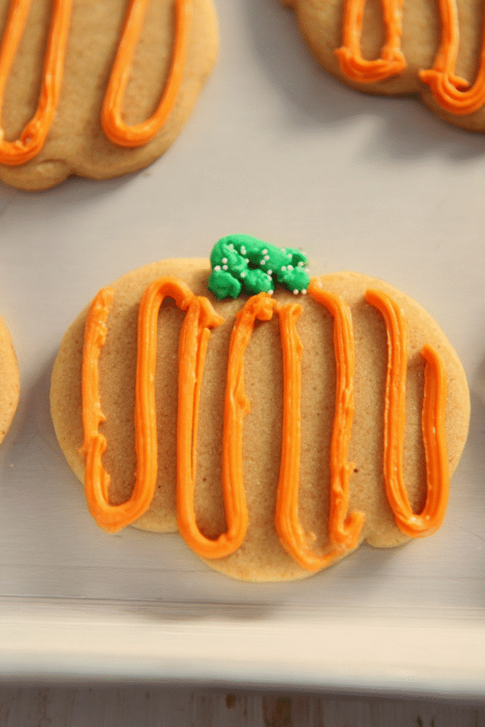 Pumpkin-shaped sugar cookie with orange frosting and green stem, perfect for pumpkin spice sugar cookies.