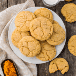 Overhead view of pumpkin sugar cookies on a white plate with pumpkin purée and milk