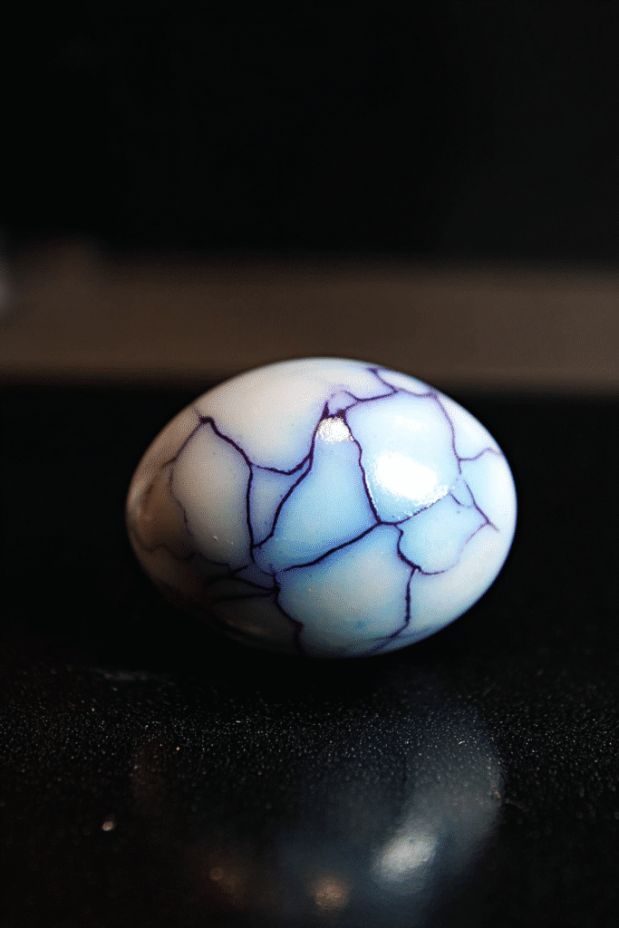 Hard-boiled egg with purple marble cracks for Halloween deviled eggs, on a black reflective surface.