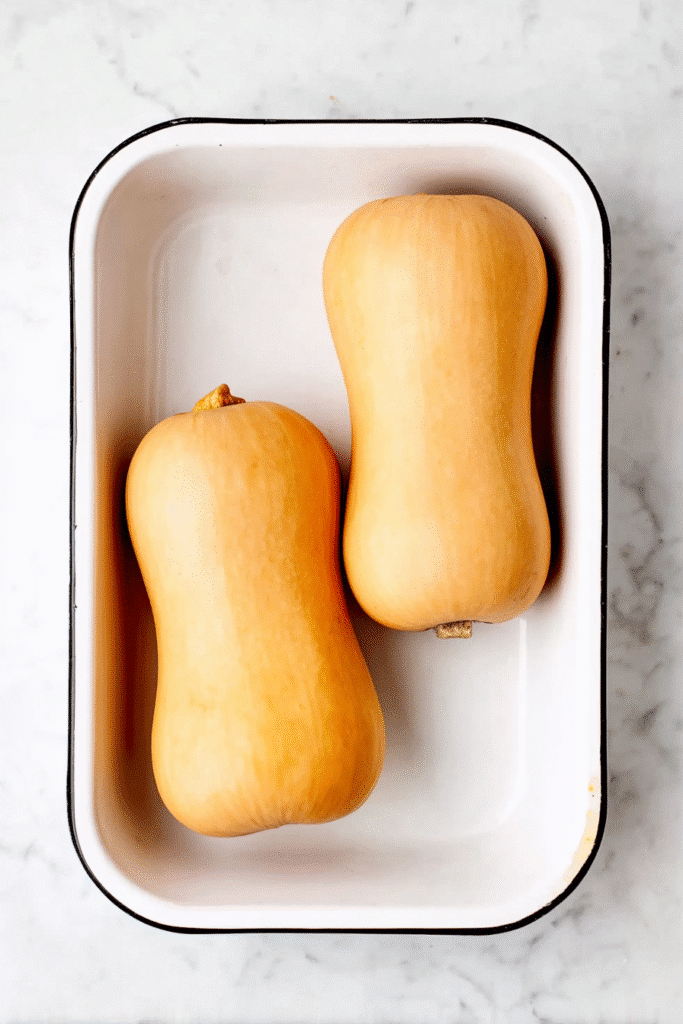 Whole butternut squash in a roasting pan prepped for Apple Sausage Stuffed Butternut Squash