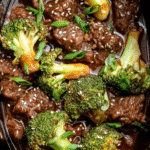 Slow cooker beef and broccoli in rich sauce with sesame seeds and green onions.