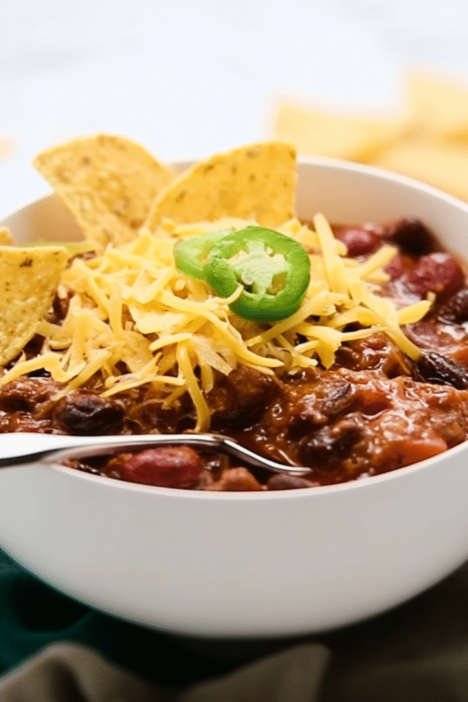 Bowl of slow cooker chili topped with shredded cheese, tortilla chips, and jalapeño.