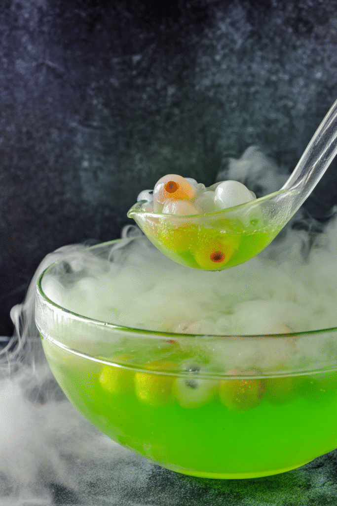 Large Halloween punch bowl with neon green drink, floating eyeballs, and dry ice smoke.