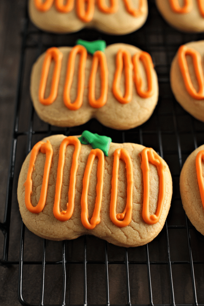 Pumpkin spice sugar cookies with orange frosting cooling on a wire rack.