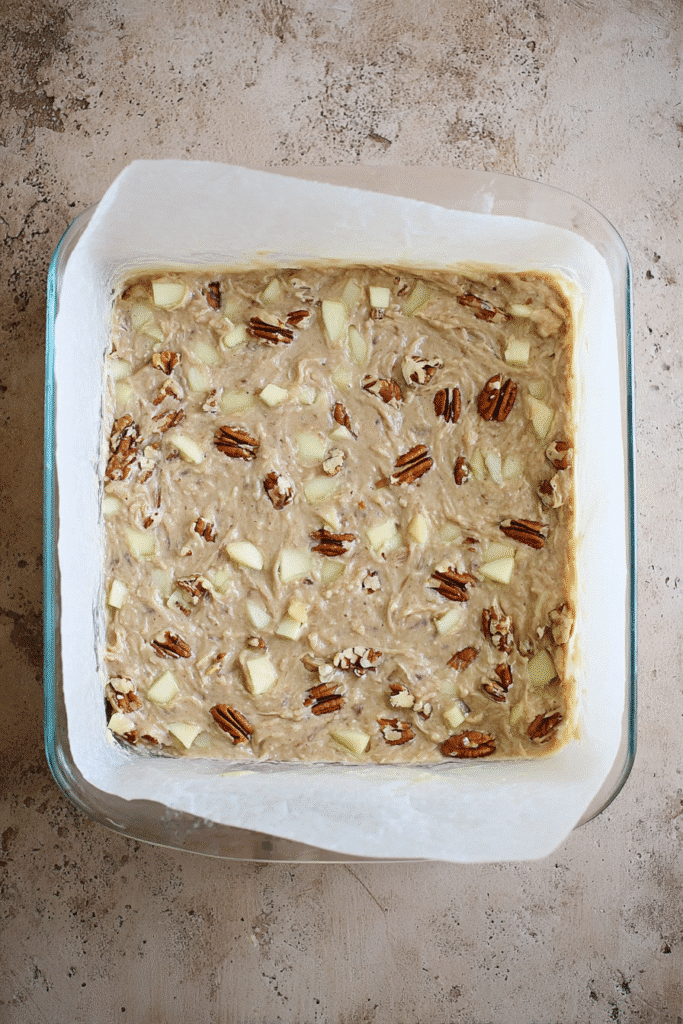 Apple brownie batter with pecans spread in a baking dish before baking