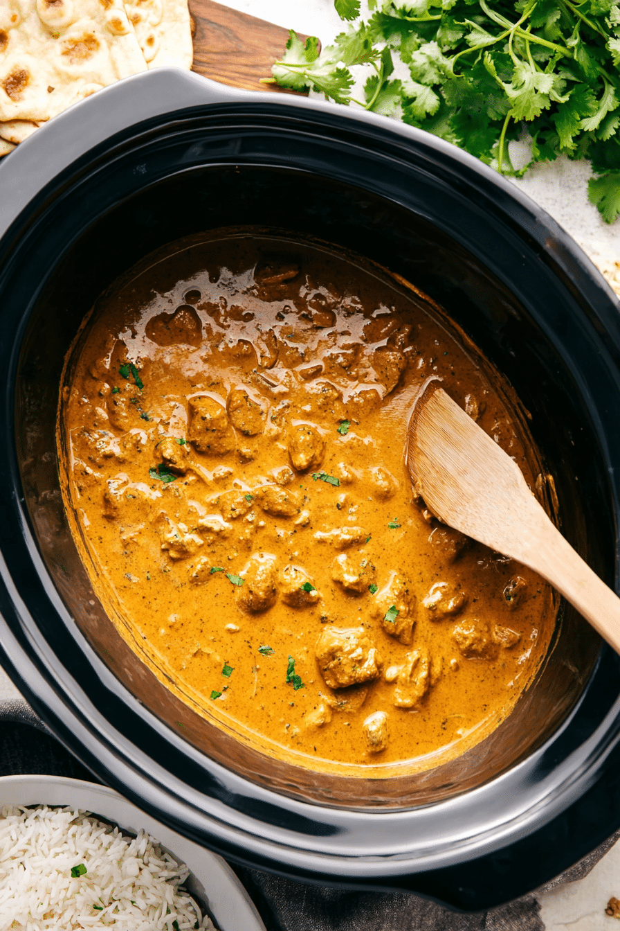 Creamy Crockpot Butter Chicken in a slow cooker with rice, cilantro, and naan bread.