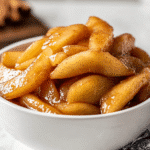 Homemade apple pie filling recipe with cinnamon-coated apples in a white bowl.