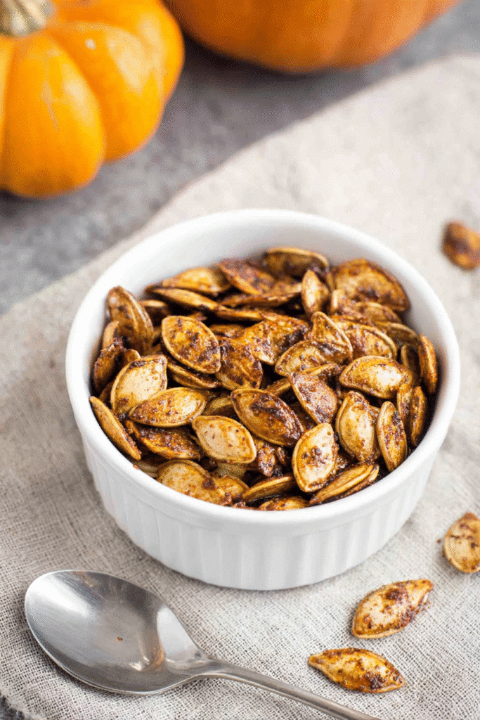 Crispy roasted pumpkin seeds recipe served in a white bowl with spices and rustic fall background.