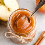 Overhead view of a jar filled with creamy healthy apple butter with spoon inside, rustic string tied around the jar.