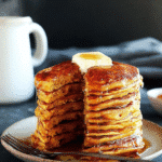 Stack of fluffy pumpkin pancakes with butter and maple syrup on a rustic plate.