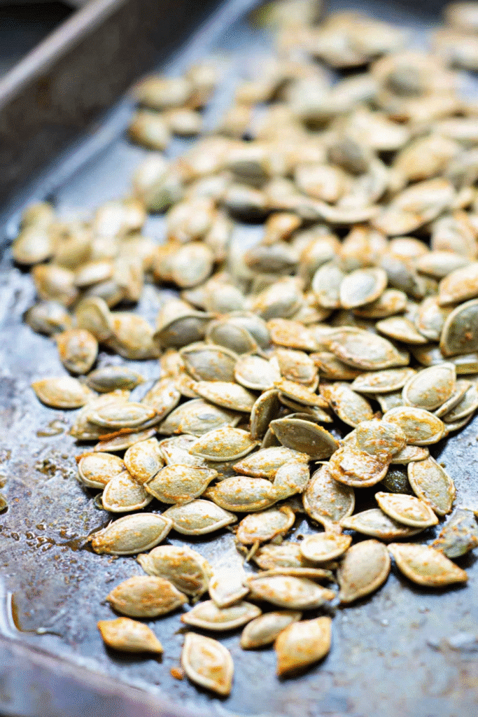 Pumpkin seeds recipe preparation with seasoned seeds spread on a baking tray before roasting.