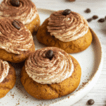 Pumpkin tiramisu cookies topped with creamy frosting, cocoa powder, and coffee beans on a white plate.