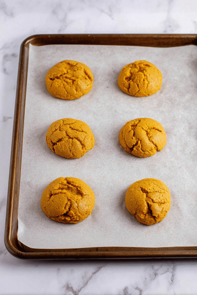 Pumpkin cookies cooling on a parchment-lined baking sheet before frosting for pumpkin tiramisu cookies.
