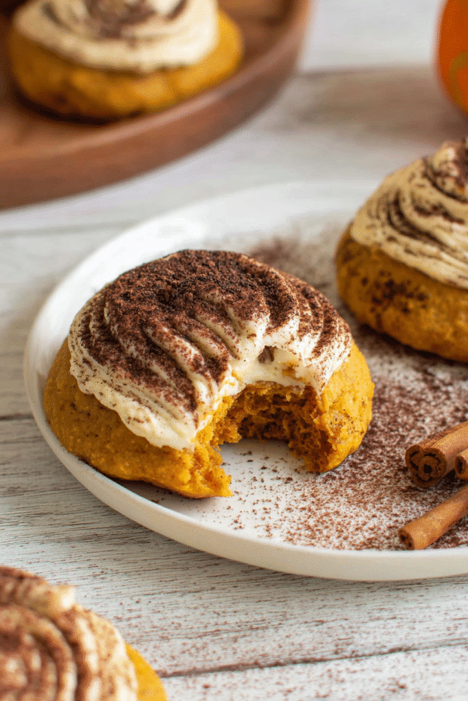 Pumpkin tiramisu cookie with creamy frosting and cocoa dusting, showing soft pumpkin interior with a bite taken out.