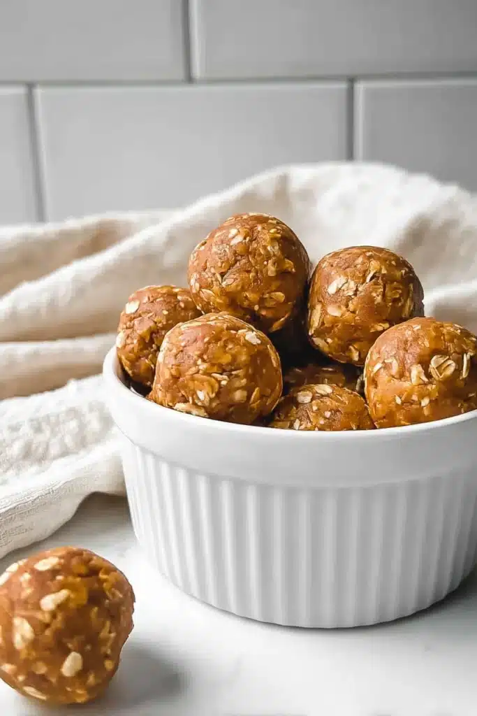 pumpkin protein balls stacked in white ramekin with oats