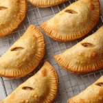 Golden mini apple pies cooling on a wire rack, featuring flaky crusts and vented tops.
