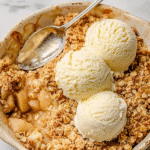 Simple apple crumble topped with vanilla ice cream in a rustic baking dish.
