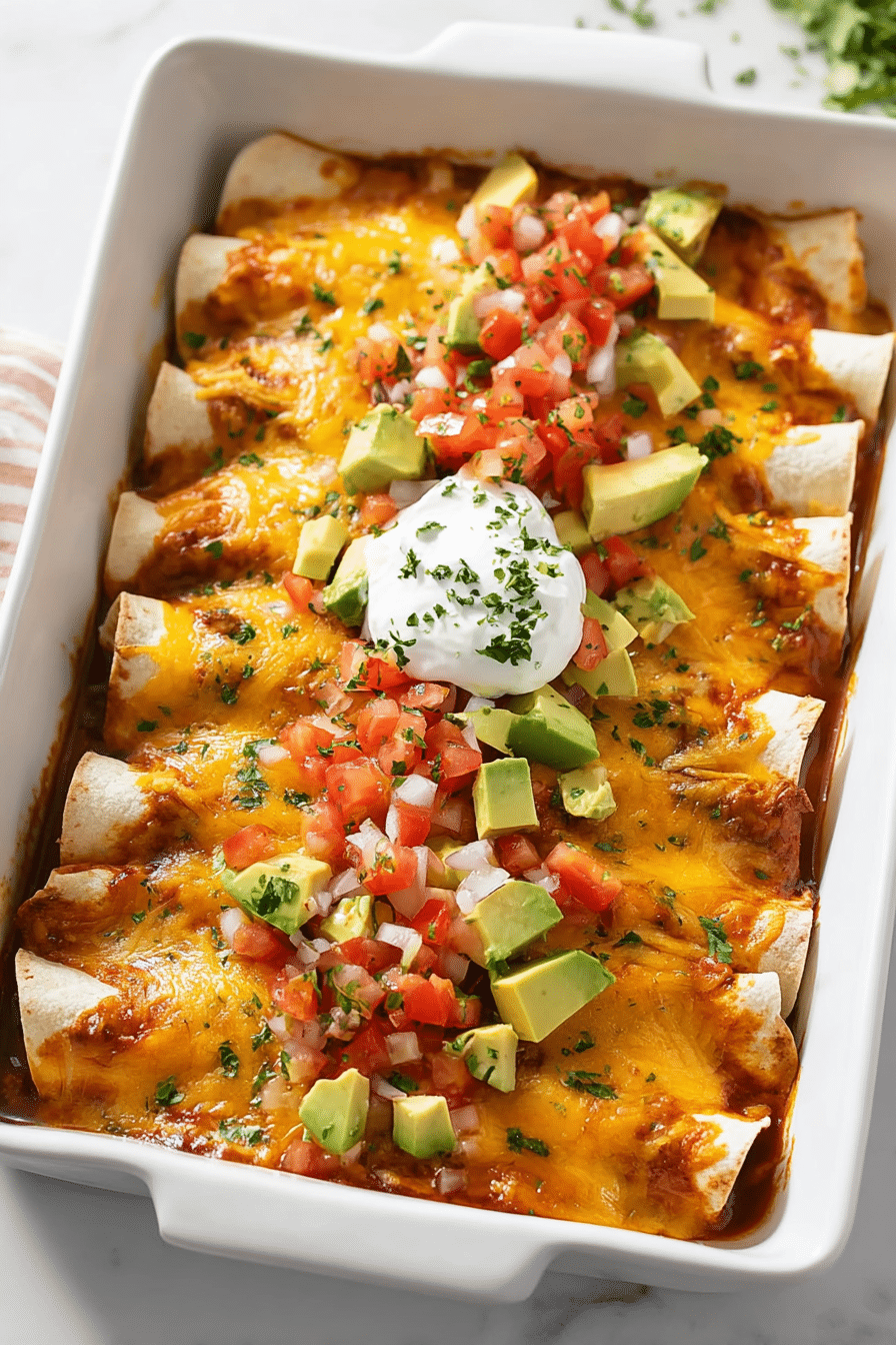 Cheesy beef enchiladas topped with avocado, salsa, and sour cream in a white baking dish.