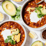 Bowls of vegetarian chili recipe topped with sour cream, avocado, cilantro, and tortilla chips.