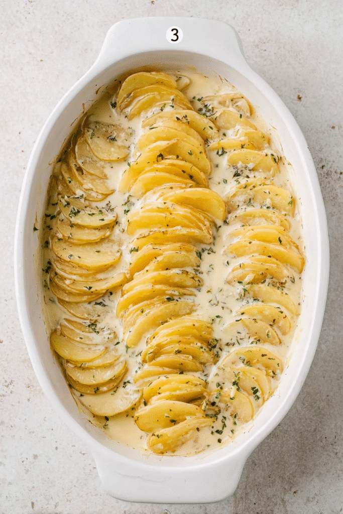 potatoes arranged in baking dish with creamy scalloped sauce