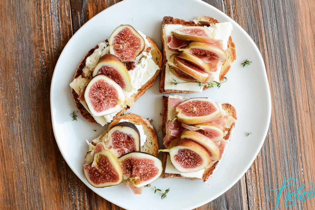 Overhead view of sliced crostini topped with figs, prosciutto, apples, and brie cheese on a white plate over a rustic wooden table