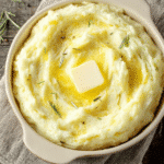 creamy rosemary garlic mashed potatoes with butter in white dish on rustic table