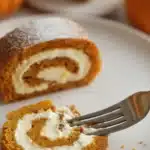 Close-up of a slice of Fall Pumpkin Spice Roll Cake with cream cheese filling and a fork.