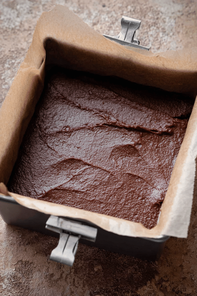 Christmas fudge batter in a baking pan lined with parchment paper. Step in the best fudge recipe.