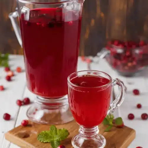 Glass pitcher and mug of Christmas morning punch with cranberries and mint on wood board
