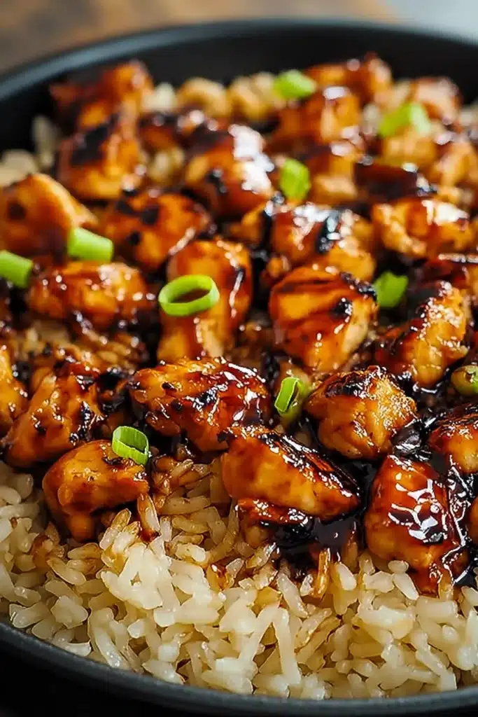 Honey BBQ chicken rice bowl. Close-up of glazed chicken pieces over rice, garnished with green onions.