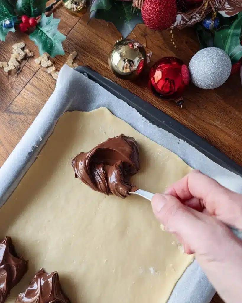 Spooning Nutella onto puff pastry with holiday decor around