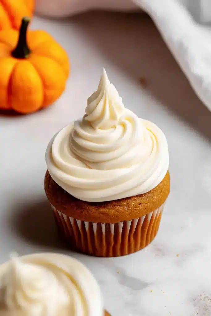 Moist pumpkin cupcakes topped with creamy swirled frosting and mini pumpkin candies, perfect for fall desserts