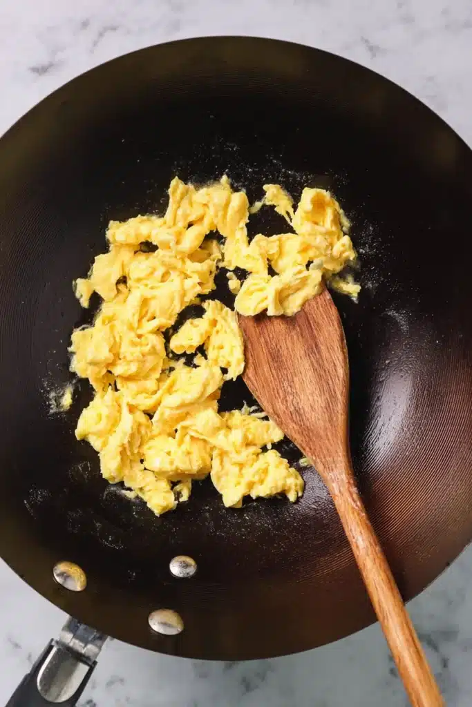 fluffy scrambled eggs cooking in a wok with wooden spoon