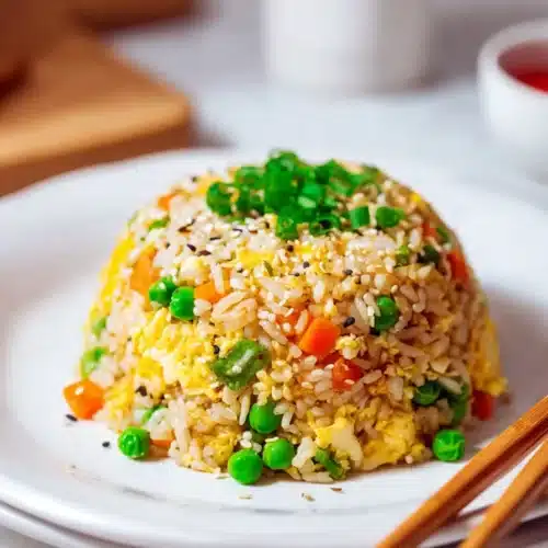 egg fried rice served in a dome shape with peas carrots and egg on a white plate
